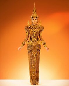 a woman dressed in an elaborate golden outfit and headdress, standing on a white surface