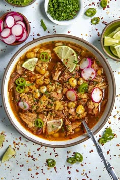 a bowl filled with meat and vegetables on top of a white table next to limes