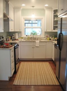 a kitchen with white cabinets and stainless steel appliances, along with an area rug on the floor