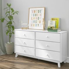 a white dresser with some books on it and a potted plant in the corner