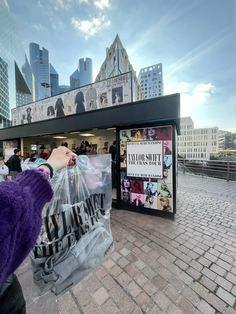 a person holding a plastic bag in front of a store on a brick sidewalk with buildings in the background