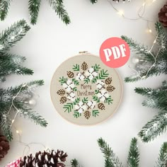 a cross stitch christmas ornament surrounded by pine cones and evergreen needles, with the text pdf on it