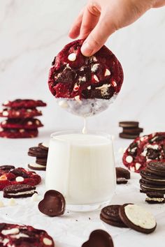 someone is dipping some kind of cookie into a glass of milk and cookies are scattered around the table