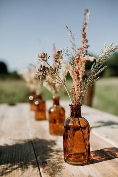 three brown vases with dried plants in them on a wooden table outside at the same time