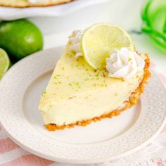 a slice of key lime pie on a white plate with two limes in the background