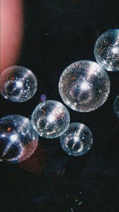 several disco balls sitting on top of a black table next to a person's hand