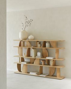 a wooden shelf with books and vases on top of it in an empty room