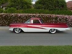 an old red and white car parked on the side of the road in front of some bushes