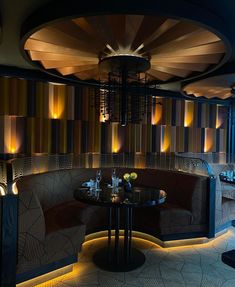 a dimly lit dining room with round tables and circular booths in the center, surrounded by wall - to - wall striped walls