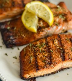 two salmon fillets on a plate with lemon wedges