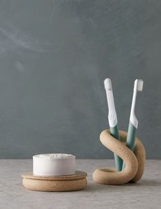 two toothbrushes sitting on top of a wooden holder next to a white cup