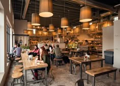 people are sitting at tables and eating in a restaurant with lots of lights hanging from the ceiling