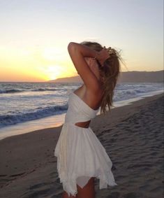 a woman standing on top of a sandy beach next to the ocean at sun set