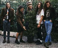 five young men standing next to each other in front of some bushes and trees,