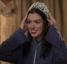 a woman wearing a tiara and smiling at the camera while holding her hair in front of her head