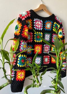 a crocheted sweater hanging on a wooden hanger next to a potted plant