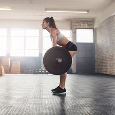 a woman holding a barbell while standing on one leg in the middle of a gym