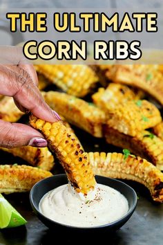 someone dipping corn on the cob into a bowl with ranch dressing and lime wedges