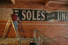 a man standing on a ladder in front of a brick wall that reads fsols for the united