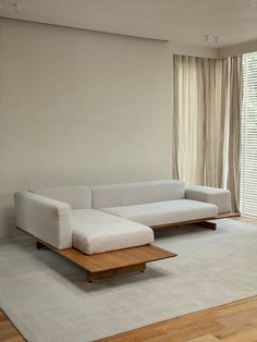 a large white couch sitting on top of a wooden table in a living room next to a window