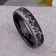 a black and silver wedding ring with trees on the inside is sitting on a rock