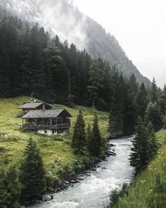 a house on the side of a mountain with a river running between it and trees