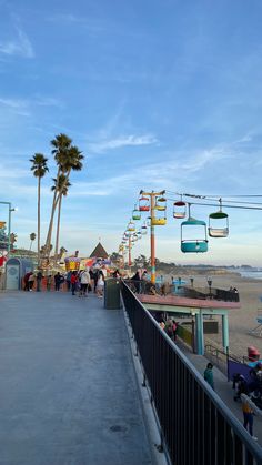 people are walking on the boardwalk at an amusement park near the ocean and beach with palm trees