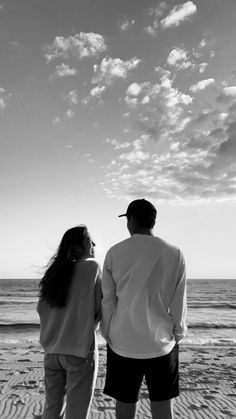 a man and woman standing on top of a beach next to the ocean under a cloudy sky