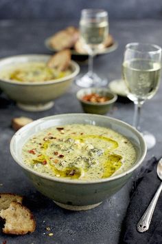 there is a bowl of soup on the table next to two wine glasses and bread