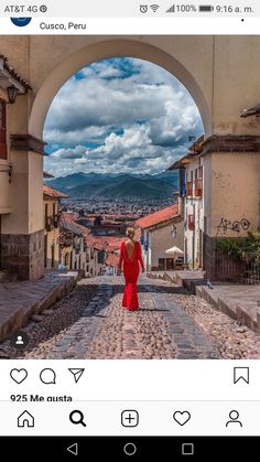 a woman in a red dress walking down a cobblestone street with mountains in the background