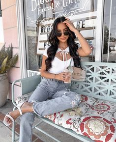 a woman sitting on a bench in front of a store window wearing ripped jeans and white top