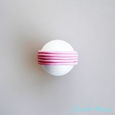 a white ball with pink bands on it sitting on a wall in front of a gray background