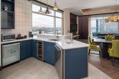 a kitchen with blue cabinets and white counter tops next to a large window overlooking the city