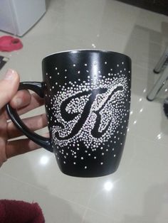 a hand holding a black coffee mug with white stars on it and the letter b