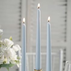 three blue candles sitting on top of a table next to white flowers and wine glasses