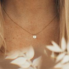 a close up of a woman's neck wearing a gold necklace with a small disc