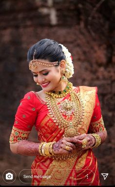 a woman in a red and gold sari holding her hands on her chest, smiling at the camera