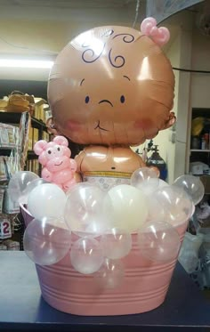 an inflatable teddy bear sitting on top of a pink bucket filled with balloons