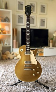 a gold electric guitar sitting on top of a carpet next to a wall mounted tv