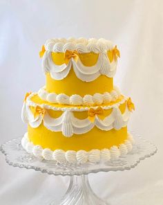 a three layer yellow and white cake on a glass stand with the top tier decorated in icing