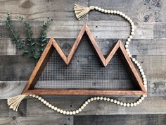 a wooden frame with beads and tassels hanging from it on a wood wall