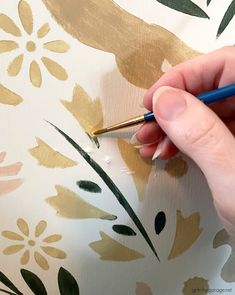 someone using a pen to paint flowers on a wallpaper with gold and green leaves