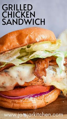 a grilled chicken sandwich with lettuce, tomato and bacon on a wooden cutting board