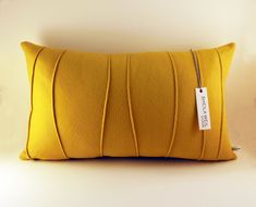 a yellow pillow with a tag hanging from it's side on a white wall