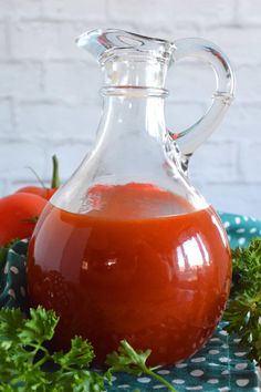 a glass pitcher filled with tomato juice on top of a blue and white checkered cloth