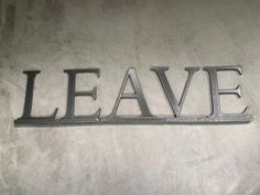 the word leave is spelled in metal letters on a gray surface with a white background