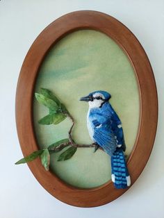 a blue bird sitting on top of a branch in a wooden frame with green leaves