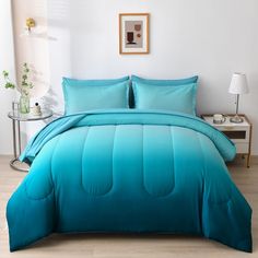 a bed with blue comforters and pillows in a room next to a lamp on a table