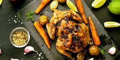 a roasted chicken with carrots, potatoes and garlic on a cutting board next to lemons