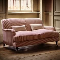 a pink couch sitting on top of a hard wood floor next to a wooden window